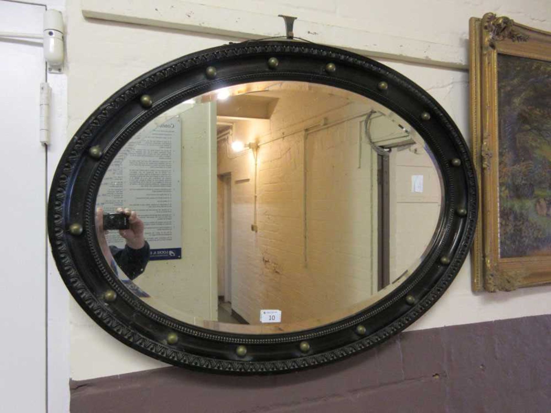 An early 20th century black framed oval bevel glass mirror with brass spheres