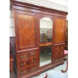 An early 20th century mahogany inlaid compactum having a bevel glass central mirrored door flanked