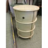 A cream painted circular cabinet with three drawers