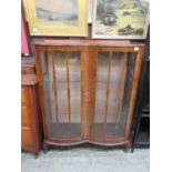 An early 20th century walnut bow front display cabinet, two glazed doors enclosing two glass shelves