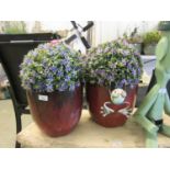 A pair of red glazed garden pots containing artificial plants