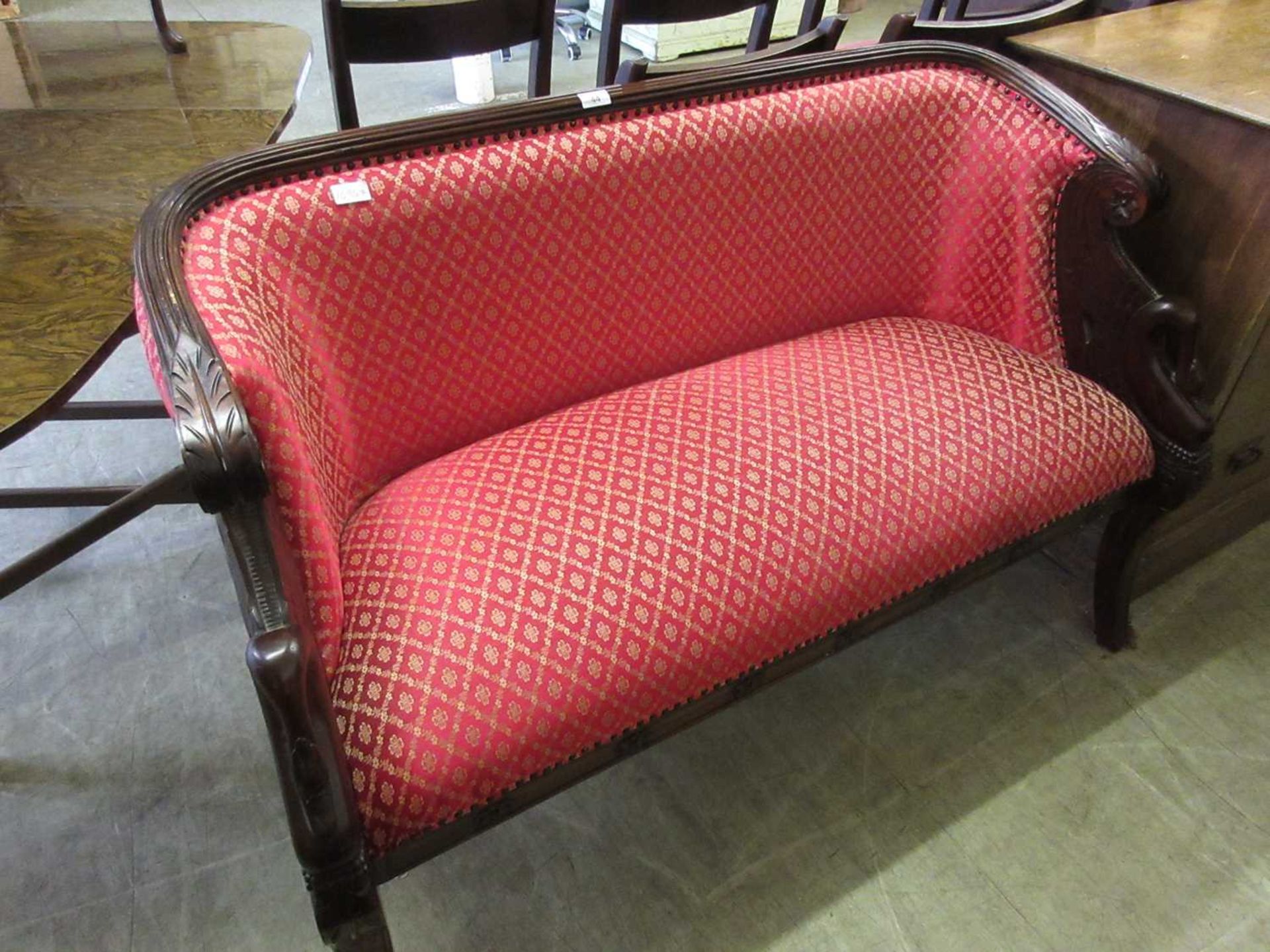 A mahogany framed two seat settee with swan carved arms upholstered in a red and gold patterned