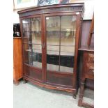 An early 20th century mahogany bow front display cabinet on squat cabriole legs with ball and claw