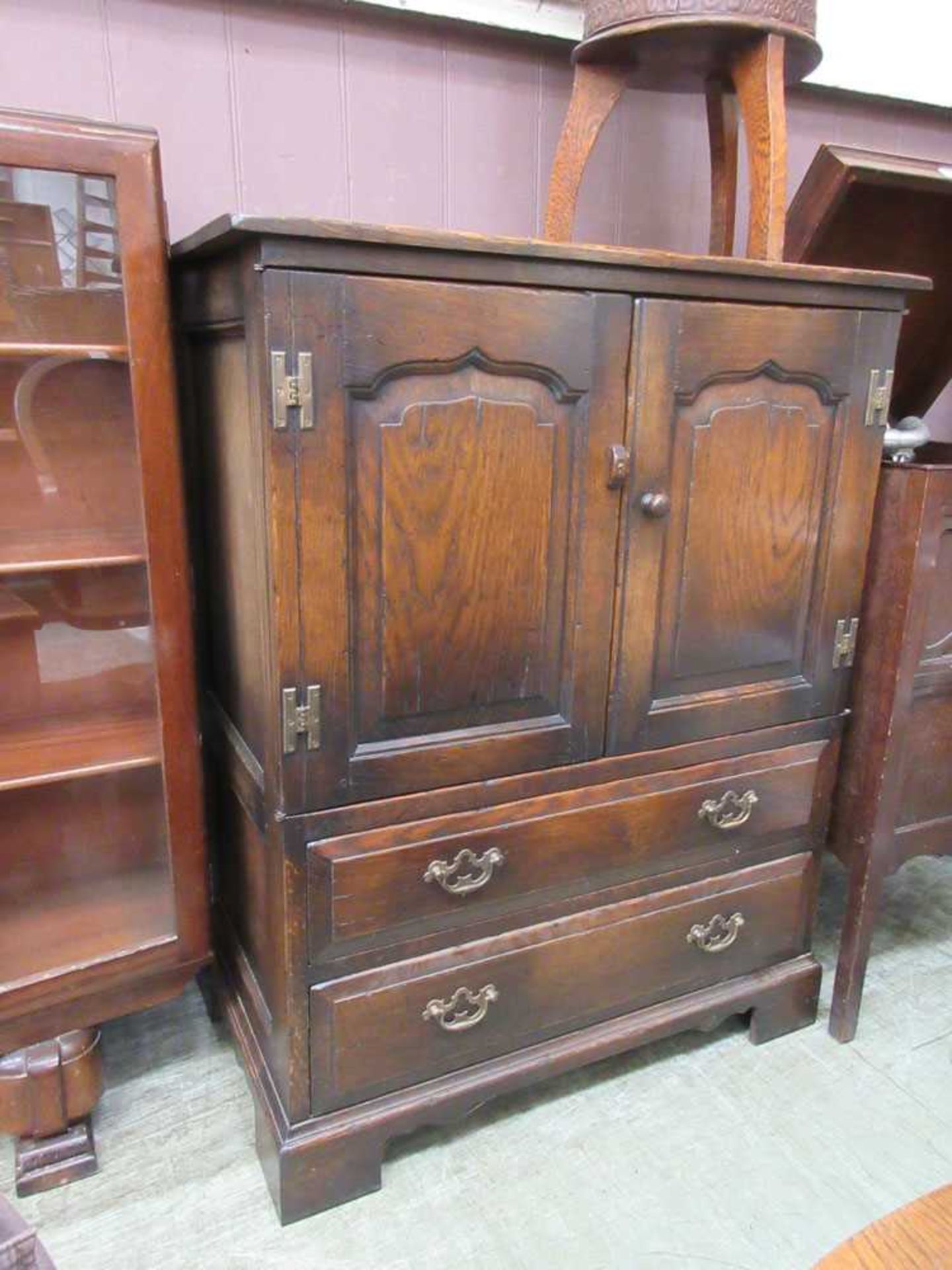 A reproduction oak cabinet having two field arch panel cupboard doors over two drawers