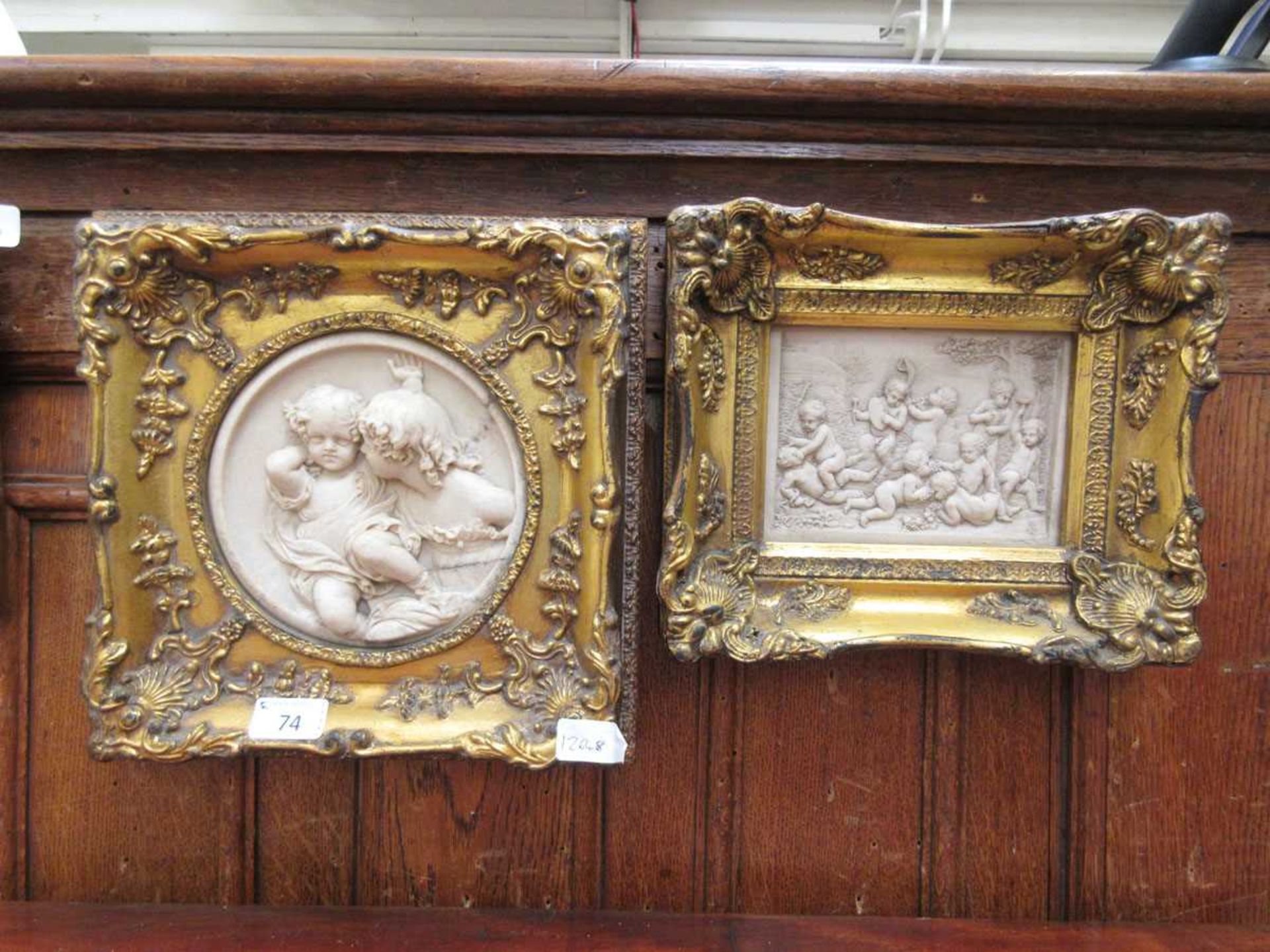 Two ornate gilt framed resin moulded relief panels of putto
