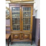 An early 20th century leaded glass two door oak bookcase with pair of cupboard doors to base