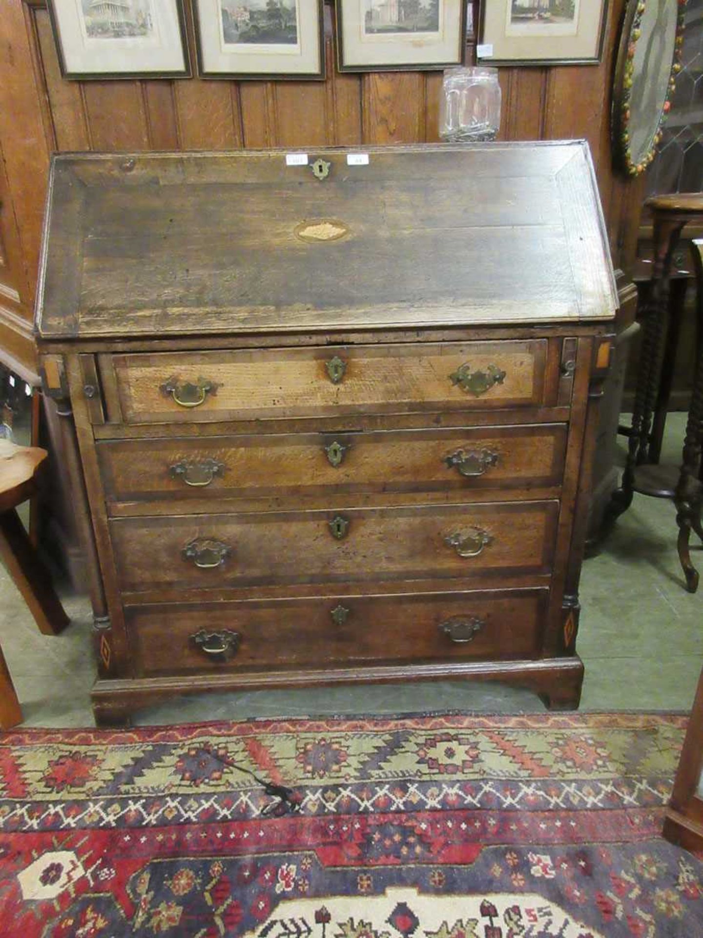 A George III oak bureau, the fall front with brass escutcheon above an inlaid marquetry conch shell,