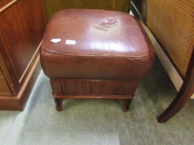 A red leatherette upholstered pouffe on carved feet