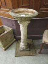 A composite stone bird bath on ornate column depicting classical figures