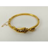 A YELLOW METAL BANGLE, probably high carat gold, set with two seed pearls, with a rope-twist cross-