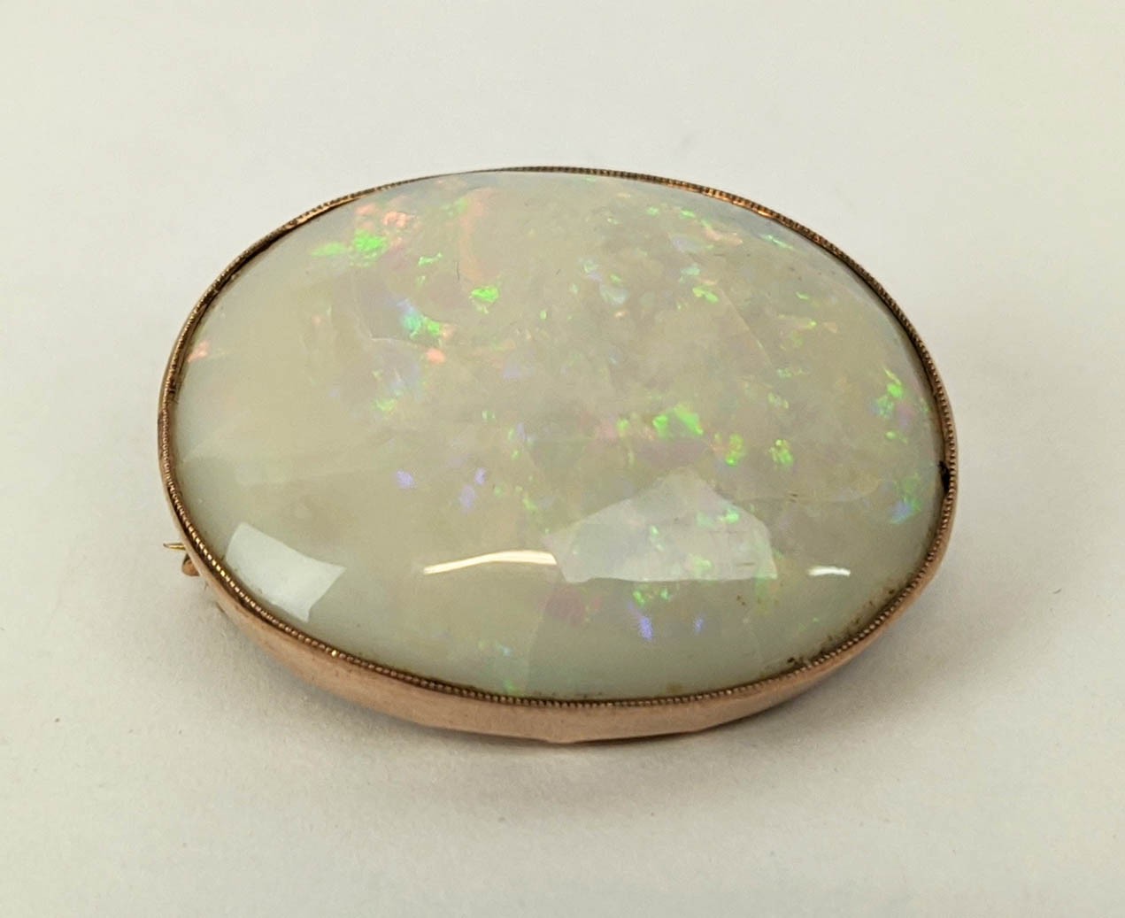 A YELLOW METAL AND OPAL SET BROOCH, probably 9ct rose gold, spiders web design to back, the oval