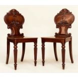 HALL CHAIRS, a pair, Regency period mahogany each with scroll carved rounded backs, panel seats