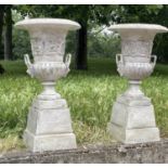 GARDEN URNS, a pair, cast iron of campana form on square stepped plinths, 46cm W x 90cm H. (2)