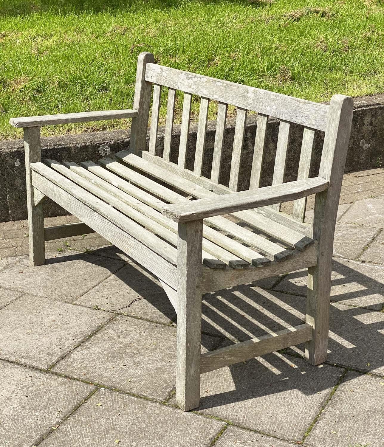 LISTER GARDEN BENCH, silvery weathered teak of slatted construction with flat top arms by R A Lister - Image 2 of 4