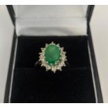 AN 18CT WHITE GOLD EMERALD AND DIAMOND DRESS RING, the central claw set emerald with an