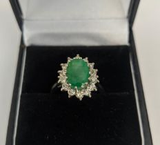 AN 18CT WHITE GOLD EMERALD AND DIAMOND DRESS RING, the central claw set emerald with an