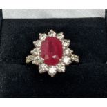 AN 18CT WHITE GOLD RUBY AND DIAMOND CLUSTER RING, with diamond set shoulders, the central oval cut