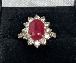 AN 18CT WHITE GOLD RUBY AND DIAMOND CLUSTER RING, with diamond set shoulders, the central oval cut