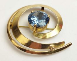 A YELLOW METAL BROOCH, SWIRL DESIGN, set with a large central blue stone, probably topaz, claw