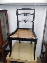 A Regency-style ebonised chair with applied brass decoration, sabre legs and wicker seat, all in the