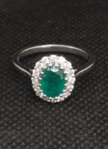 An 18ct white gold emerald and diamond cluster ring. Oval-cut emerald 1.18ct. Round brilliant cut