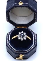 A yellow metal, sapphire, and diamond floral cluster ring, set with a dark blue round-cut sapphire