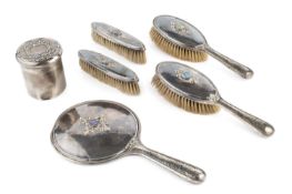 A silver Arts & Crafts style six piece dressing table set, comprising hand mirror, two hairbrushes