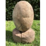 An ovoid stone sculpture on a rounded sandstone base