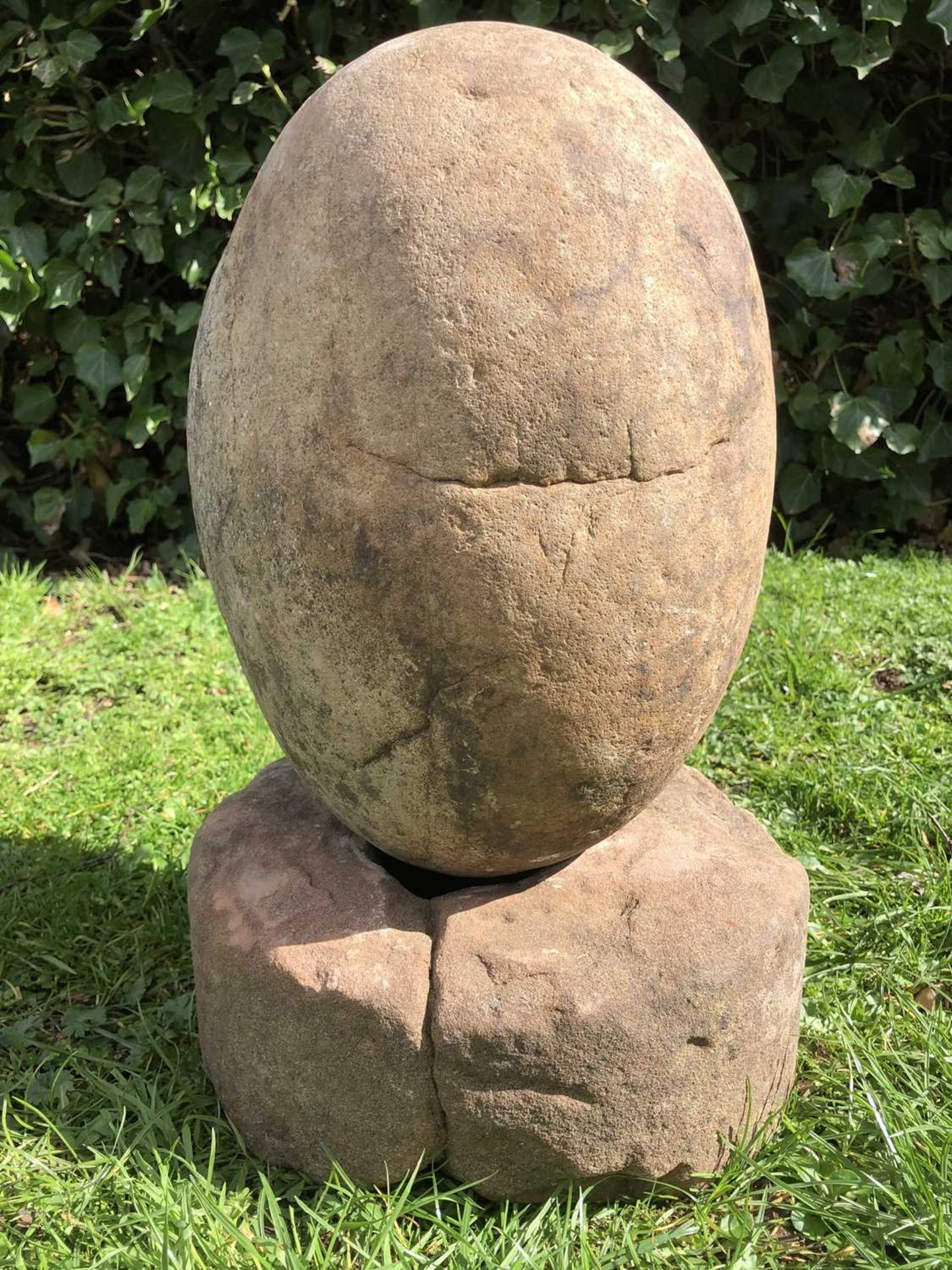 An ovoid stone sculpture on a rounded sandstone base