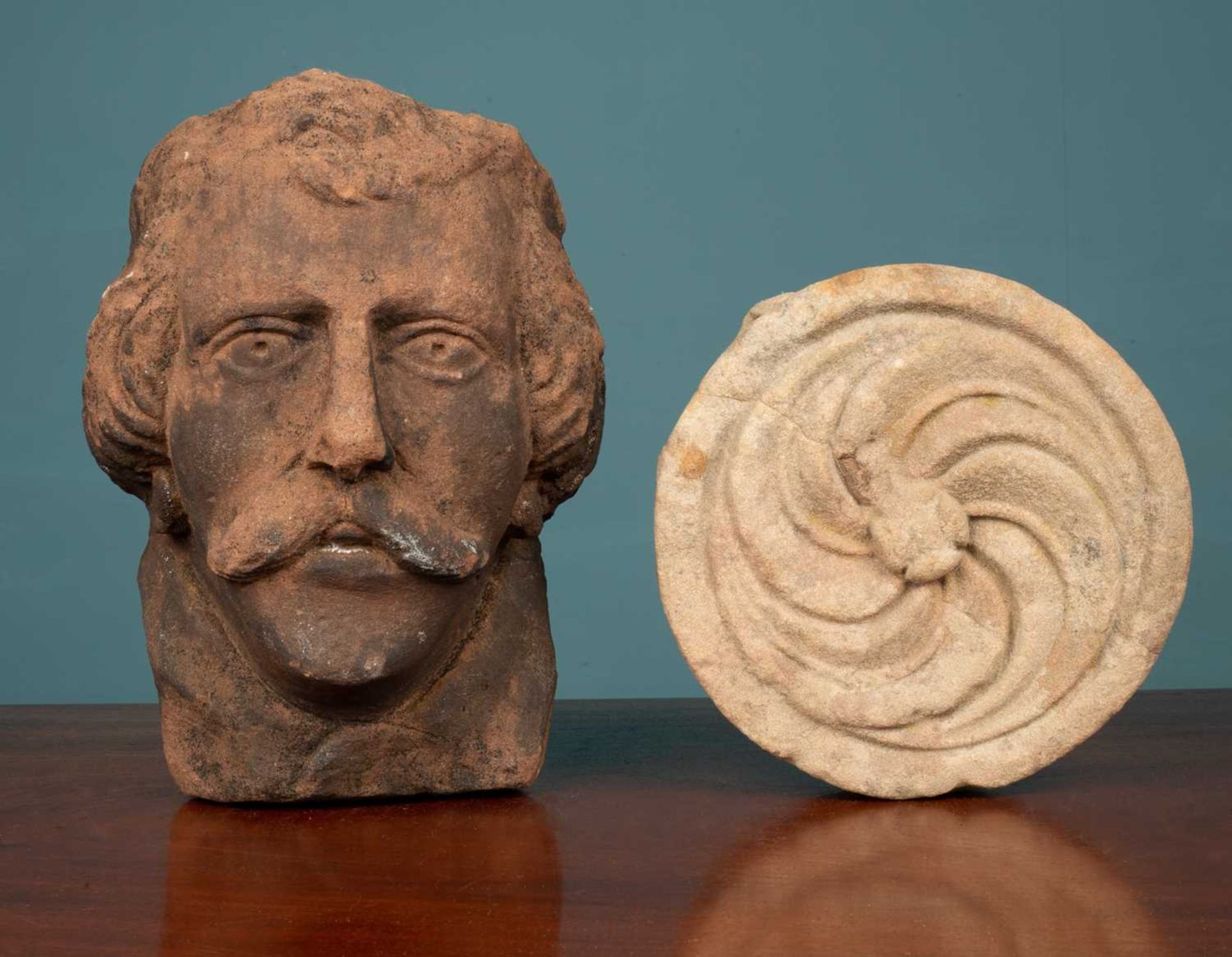 A carved sandstone head from Cockermouth, and a round carved stone element