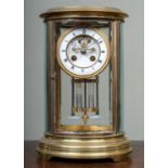 A French oval brass four-glass mantle clock with bevelled glazed panels, the two-part dial with