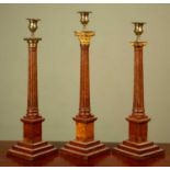 A group of three similar Masonic candlesticks each with fluted columns beneath differing capitals,