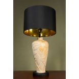 A carved soapstone lamp, with carved foliate design and a black circular lampshade, on a black base,