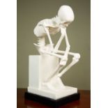 A composite resin sculpture of a skeleton seated on a plinth, 48cm high together with a resin