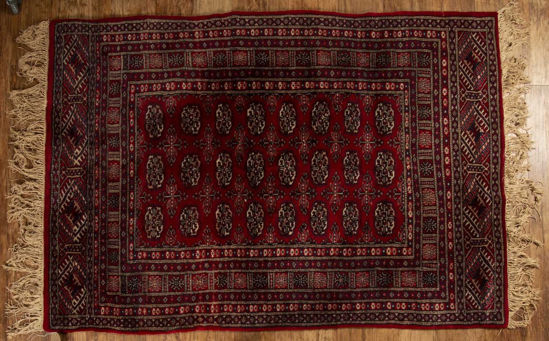 Red ground rug Pakistan, with a panel of elephant foot designs, 121cm x 172cmWith some light wear.