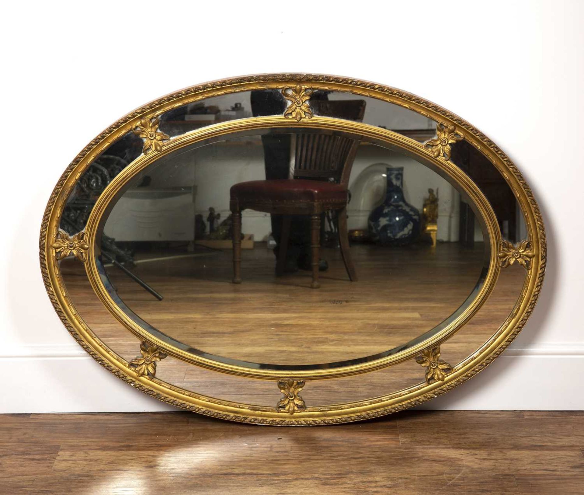 Oval gilt plaster wall mirror 19th Century, with ribbon border and carved leaf mounts, 118cm wide,