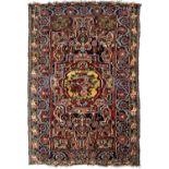 An antique Persian polychrome woollen rug with a central flower motif and geometric decoration.