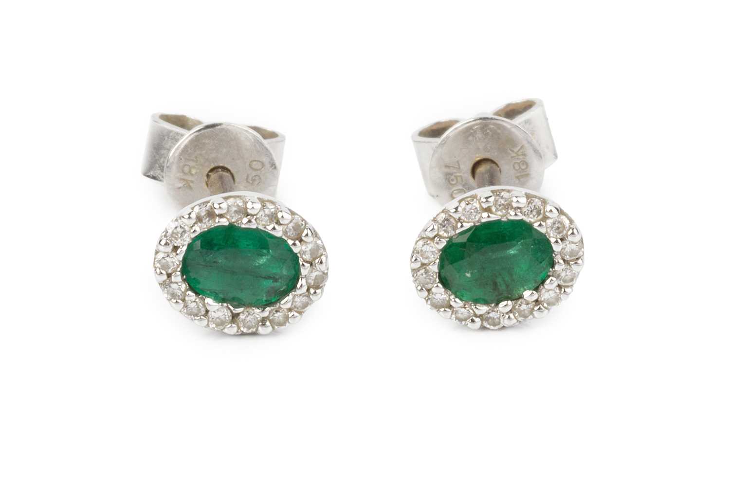 A pair of emerald and diamond cluster ear studs, each oval mixed-cut emerald bordered by round