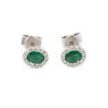 A pair of emerald and diamond cluster ear studs, each oval mixed-cut emerald bordered by round