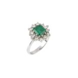 An emerald and diamond cluster ring, the rectangular step-cut emerald claw set within a border of