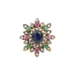 A diamond and vari gem-set cluster brooch, centred with an oval cabochon sapphire in claw setting,