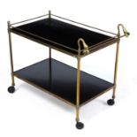 An early 20th century two tier brass tea trolley with swan neck finials, lacquered inset trays and
