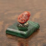 Carved coral ram's head desk paperweight attached with a brass fitting on a rectangular malachite