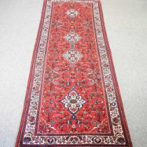 A Persian runner, with floral designs, on a red ground, 300 x 108cm