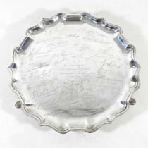 An early 20th century silver salver, of circular piecrust shape, on three hoof feet, engraved with