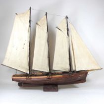 An early 20th century wooden model of a three masted schooner, with sails and rigging, on a wooden