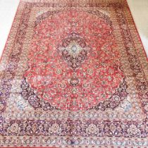 A Kashan woollen carpet, with a central medallion and foliate design, on a red ground, 390 x 290cm