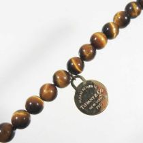 A Tiffany & Co. tiger's eye single strand bead bracelet, suspended with an 18 carat gold Tiffany