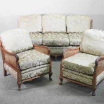 A 1920's walnut single cane bergere suite, with green floral cushions, comprising a sofa and pair of