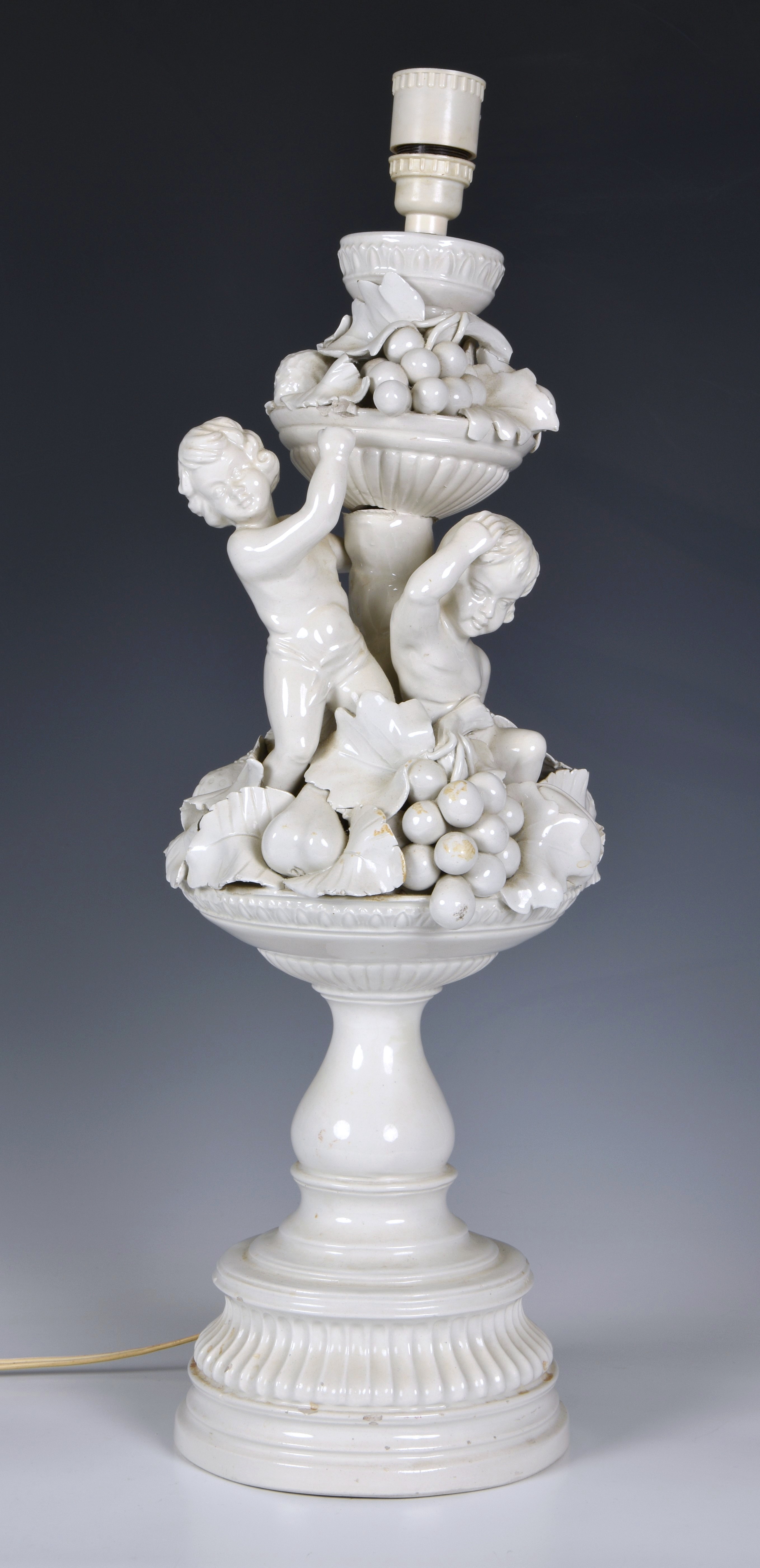 An Italian white glazed pottery table lamp, mid-20th century, modelled as two cherubs seated on an